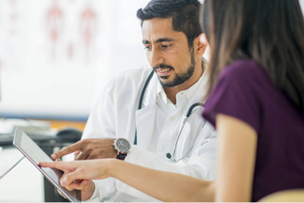 Young dentist with a black beard sharing information from a tablet with a young woman